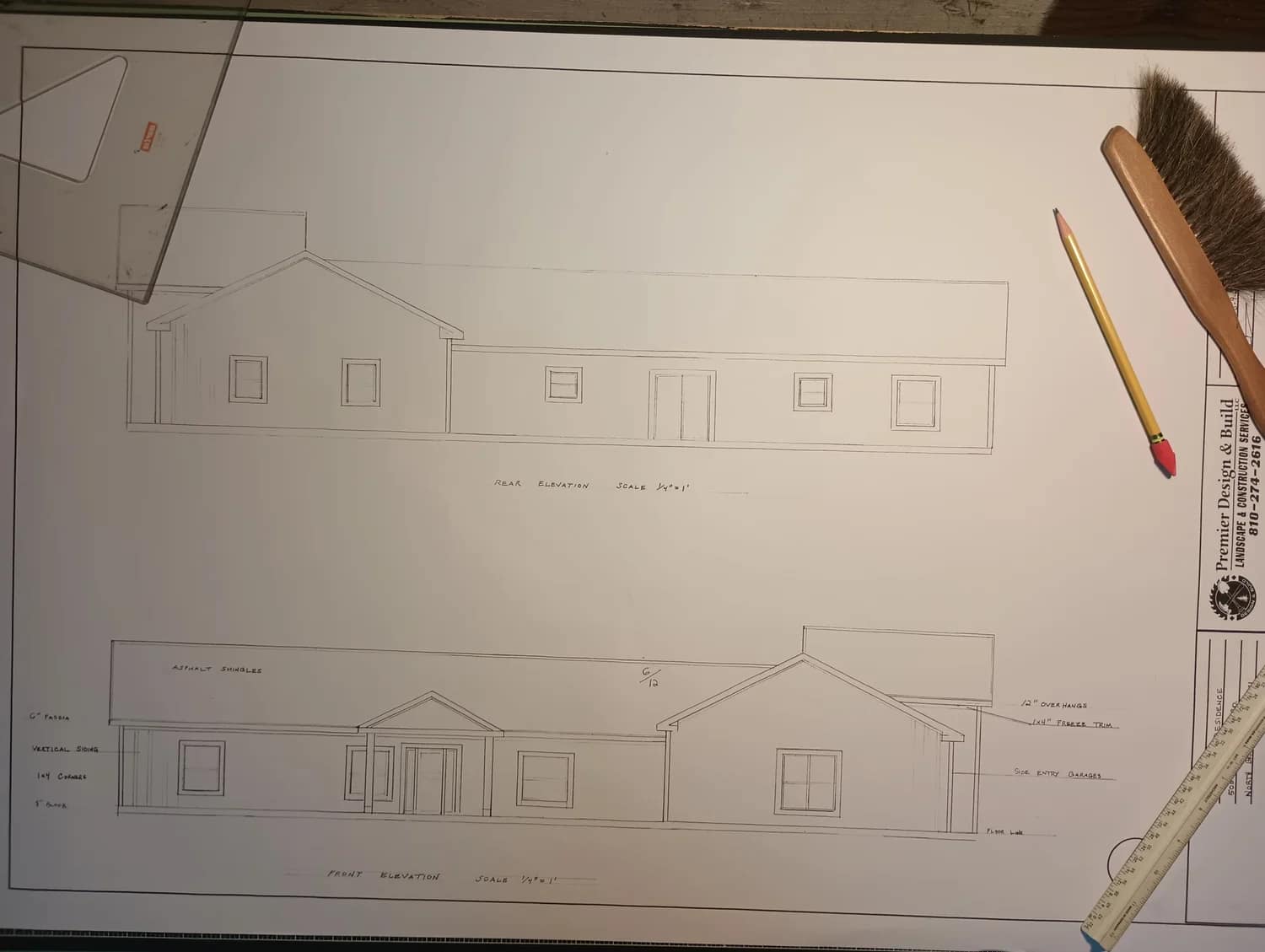 An architectural blueprint showing two elevations of a house, with a pencil, a wooden ruler, a set square, and a small broom placed around the drawing. The image is lit from above.